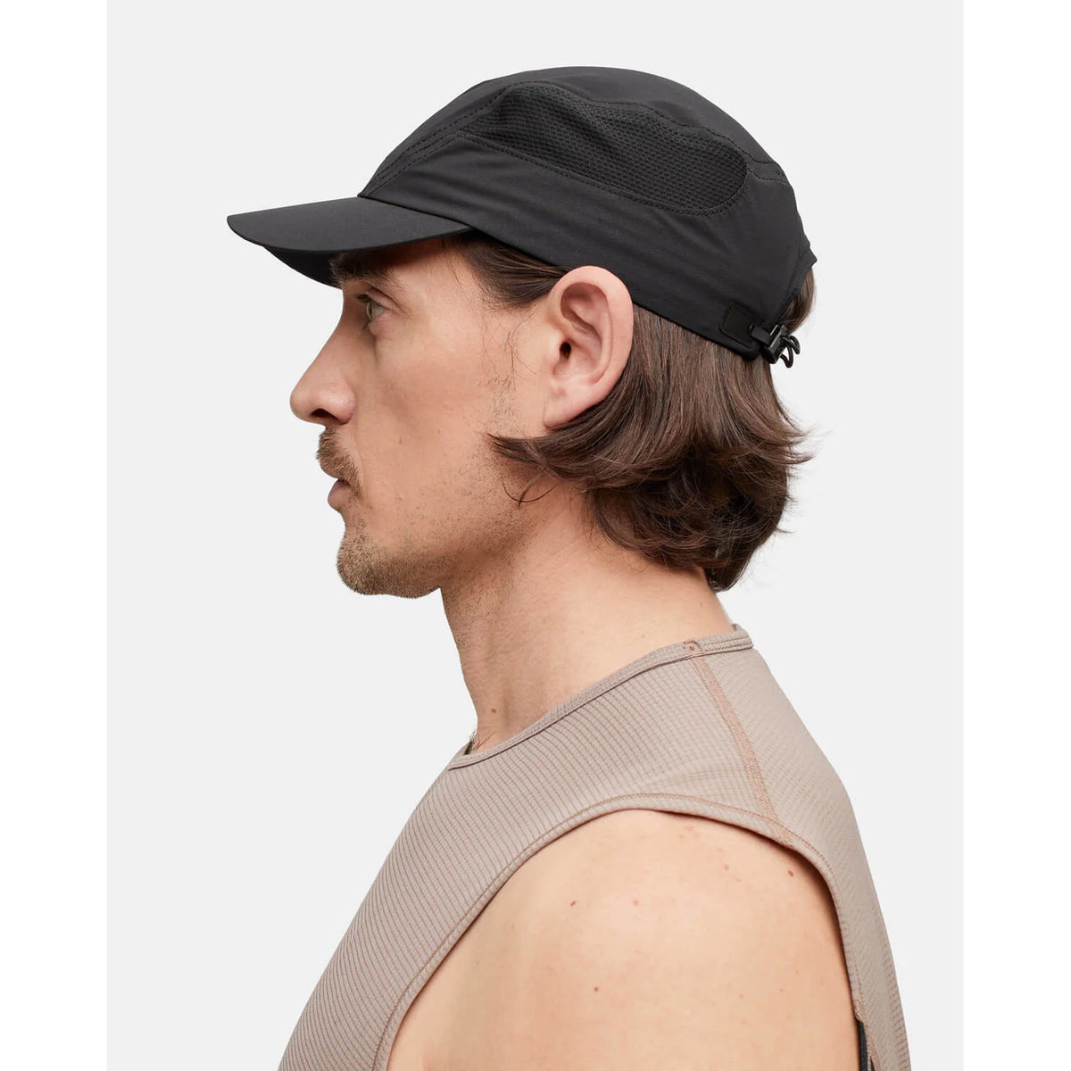 A person with shoulder-length brown hair wears the Portal Planar Lightweight Cap in Black Beauty, featuring an adjustable fit and breathable design, along with a sleeveless beige top. They are shown in profile facing left against a plain white background.