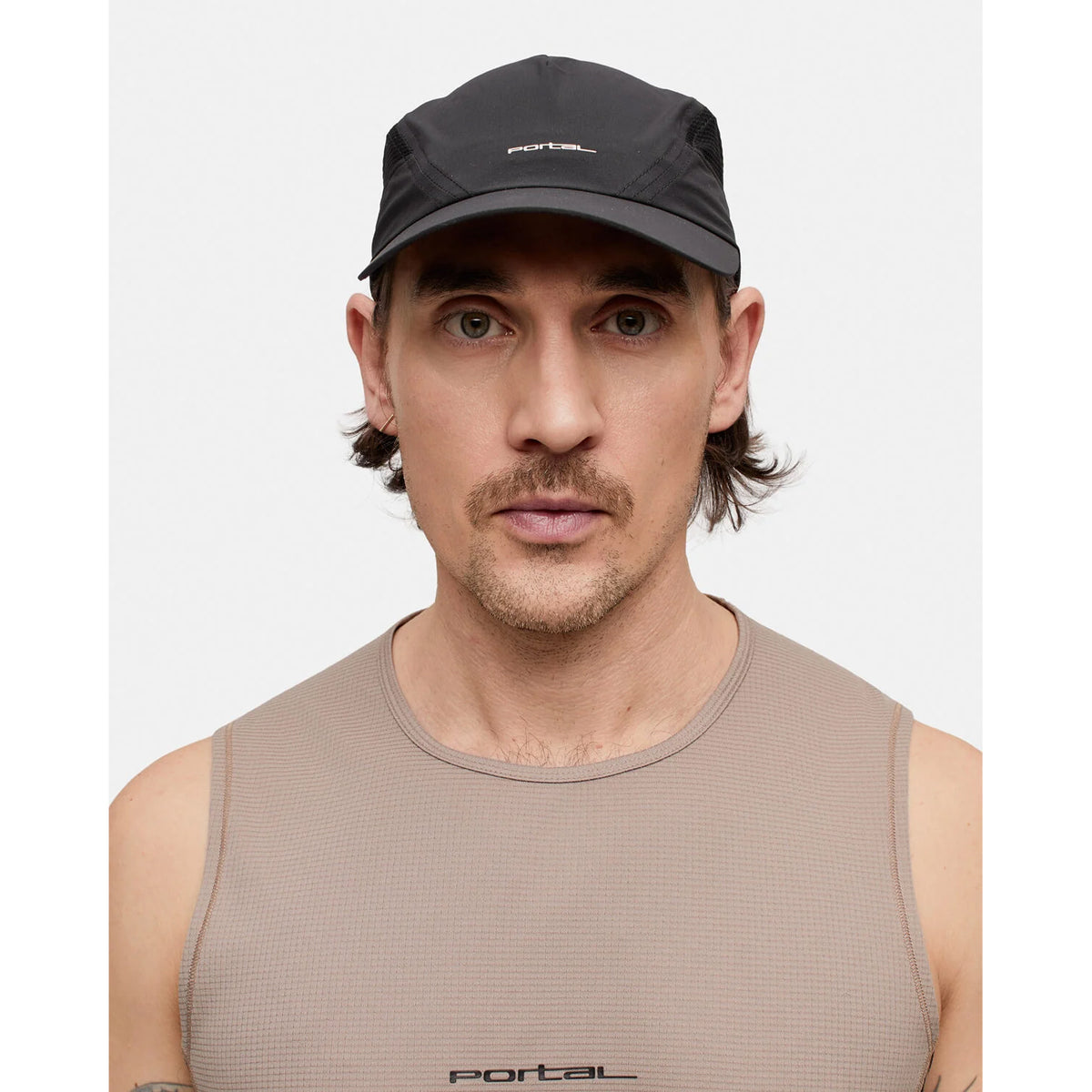 A man with a mustache and light stubble wears the Portal Planar Lightweight Cap in Black Beauty and a beige sleeveless shirt, both branded with the Portal logo. Ideal for active use, the breathable cap ensures lightweight comfort as he faces forward against a plain white background.
