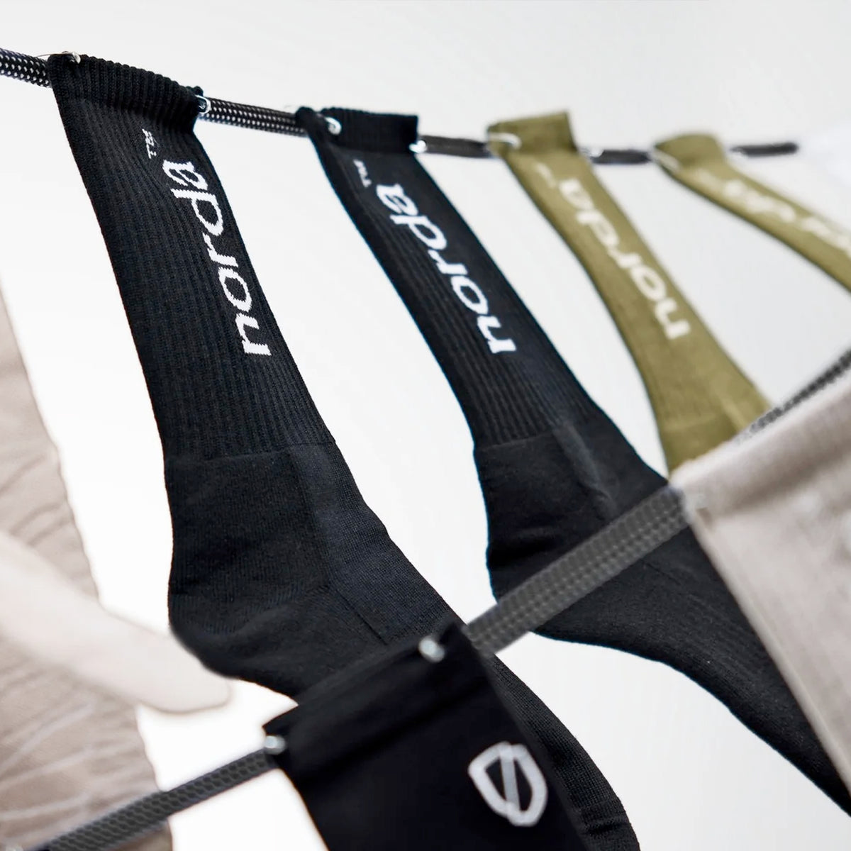 A close-up of black and green Norda branded socks hanging on a drying rack, viewed from an upward angle.