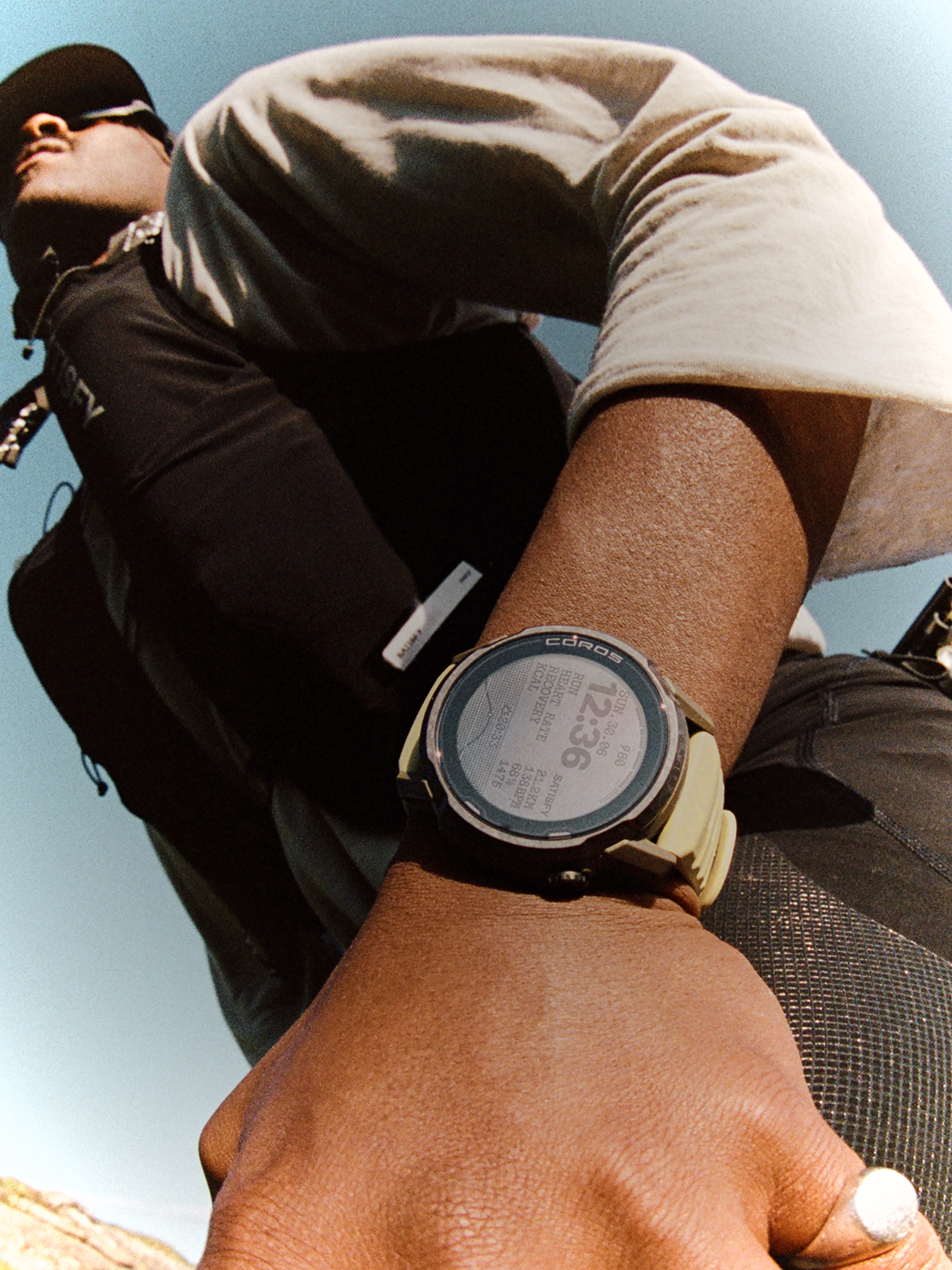 A person wearing a sports watch outdoors, displaying exercise stats. The person is dressed in athletic clothing, and the sky is clear in the background. The photo is taken from a low angle, focusing on the watch and hand.