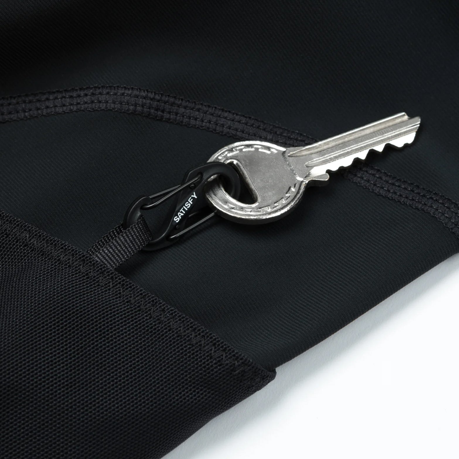 Satisfy TechSilk Evo 9 Inch Half Tights Black close-up of left-side cargo mesh pocket showing integrated mini S-Carabiner for securing keys and valuables during running