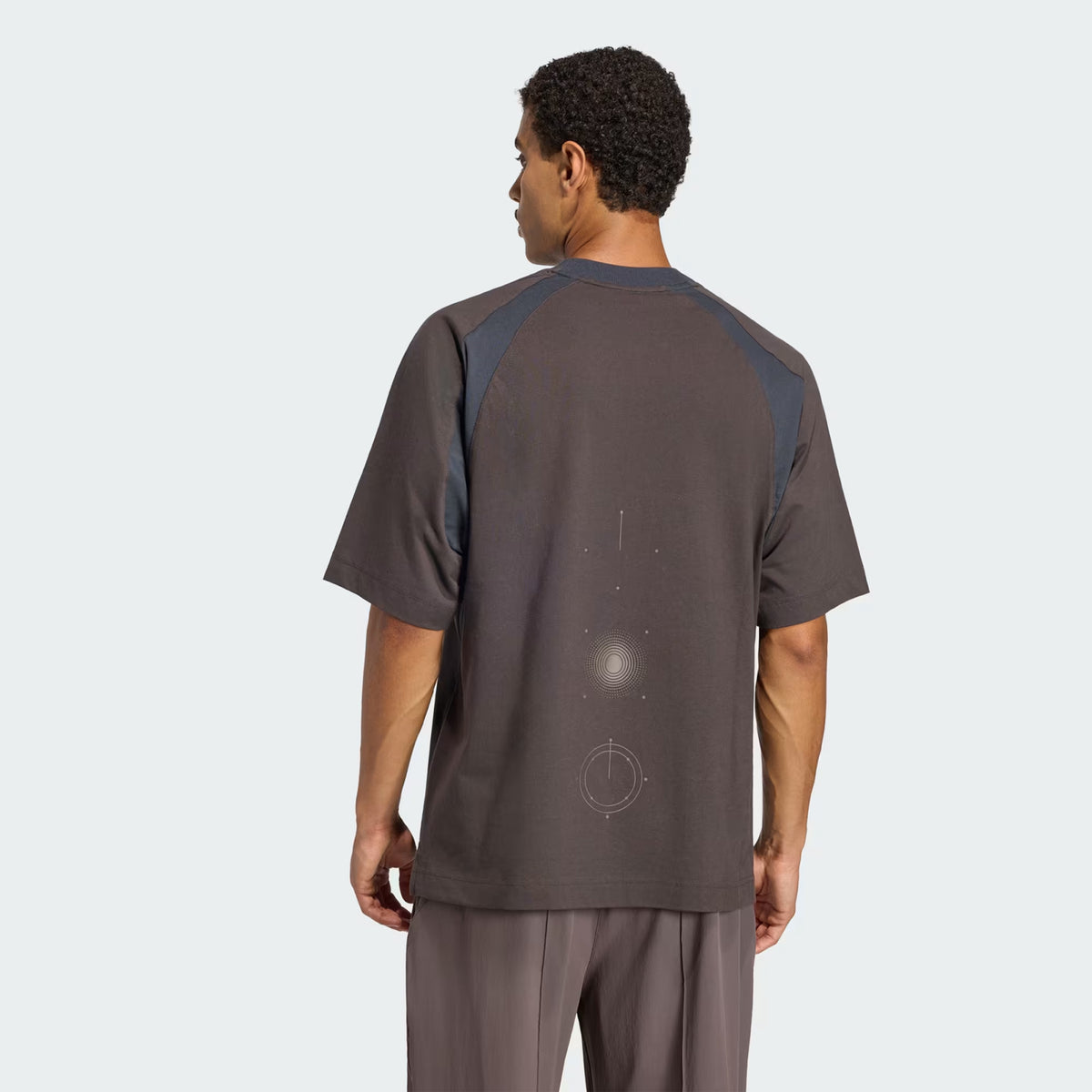 Back view of a Unisex H.Koumori Tee Night Brown / Night Grey running tee in brown with grey shoulder panels and a faint circular graphic on the back.