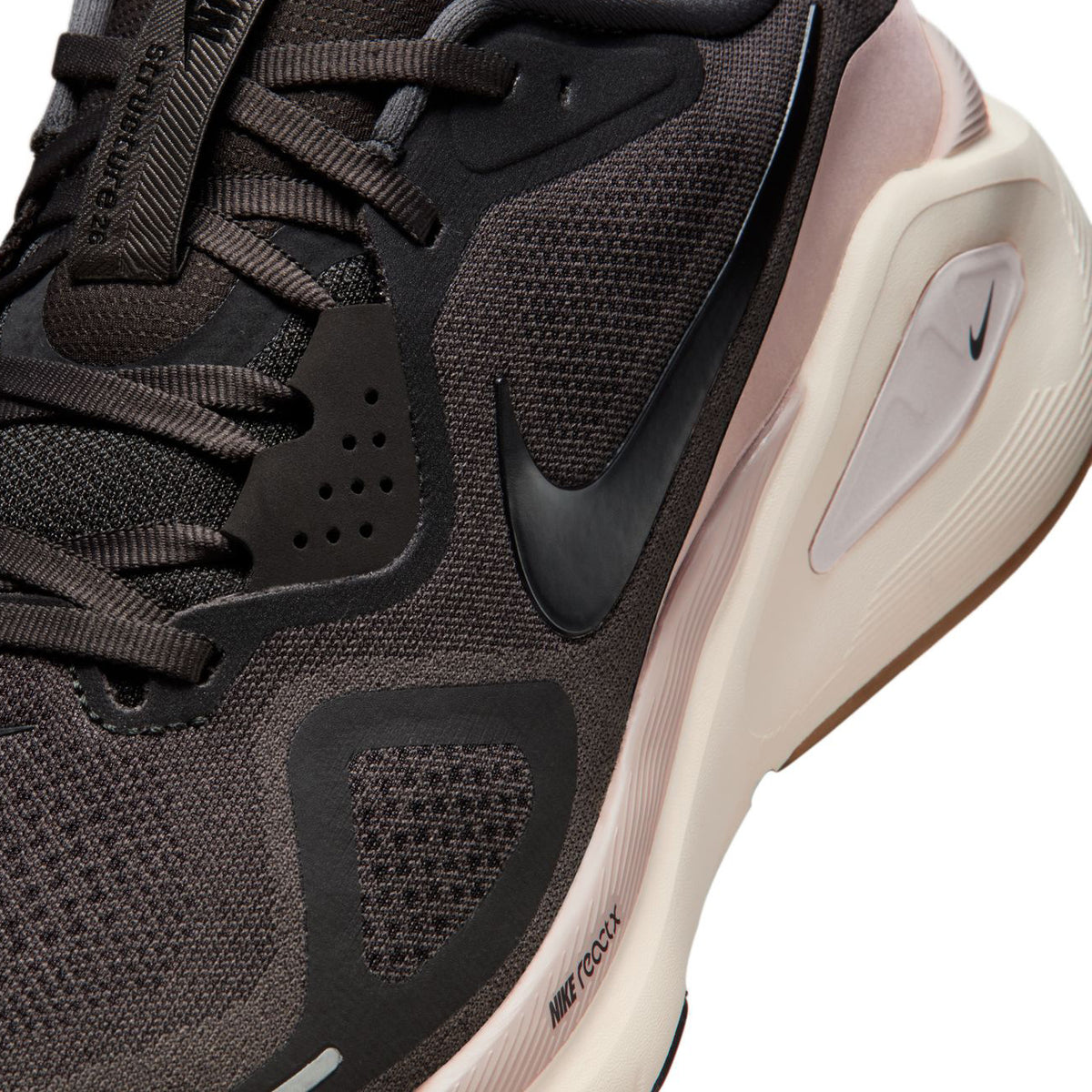 Close-up of a black and beige Nike running shoe, showing the swoosh logo, textured fabric, laces, and cushioned sole with Nike React text visible on the side.