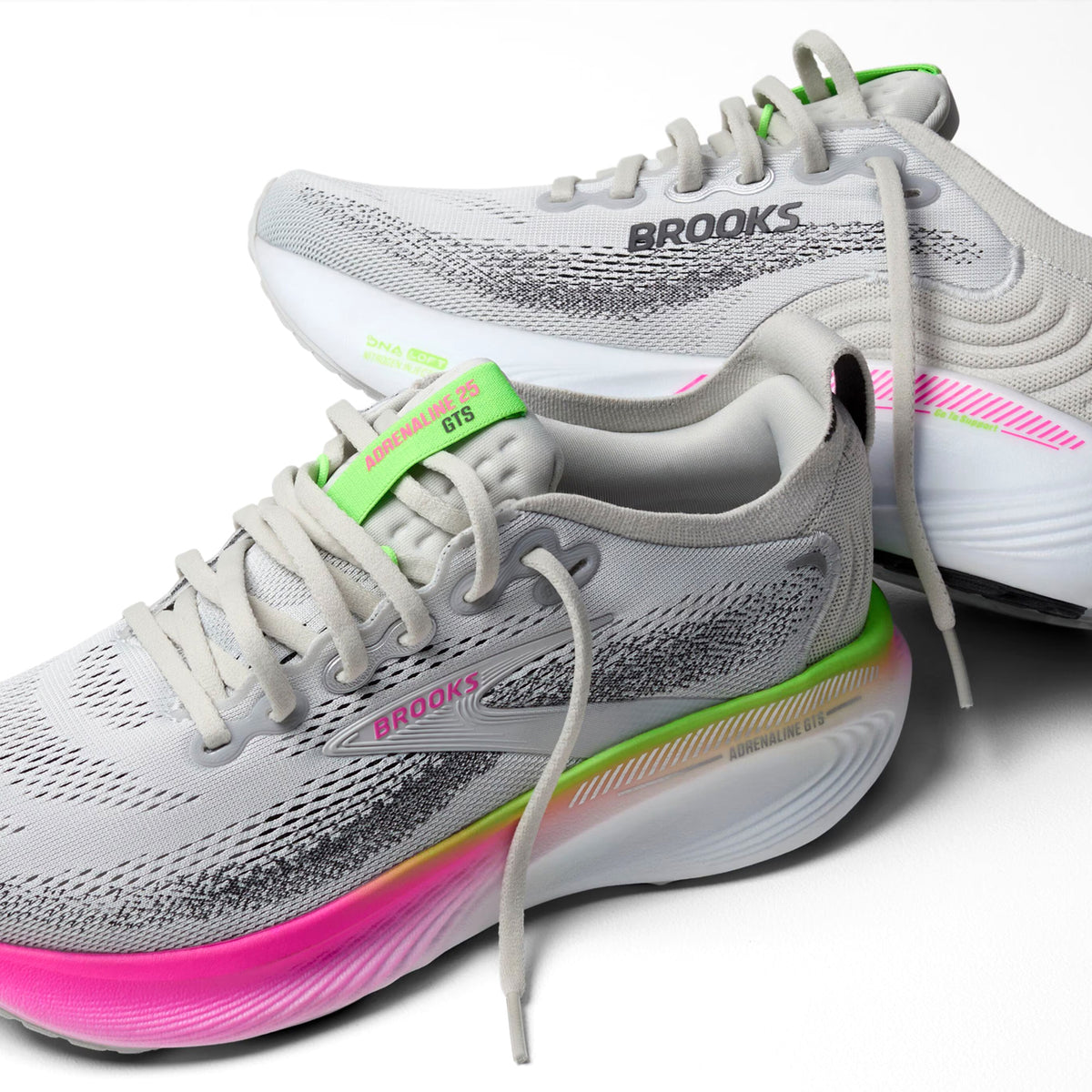 A pair of light gray Brooks running shoes with neon green, pink, and yellow accents, featuring a thick, gradient sole and mesh uppers, displayed against a white background.