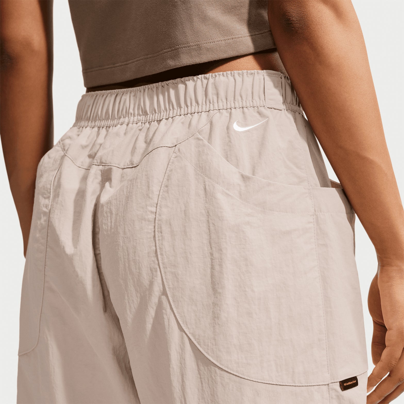 A person wearing the Nike Women’s ACG Dolomiti Trousers in Cream II / Light Orewood Brown / Summit White, shown from the back waist down, featuring side pockets and an elastic waistband—ideal for those who prefer easygoing comfort over more rugged hiking pants.