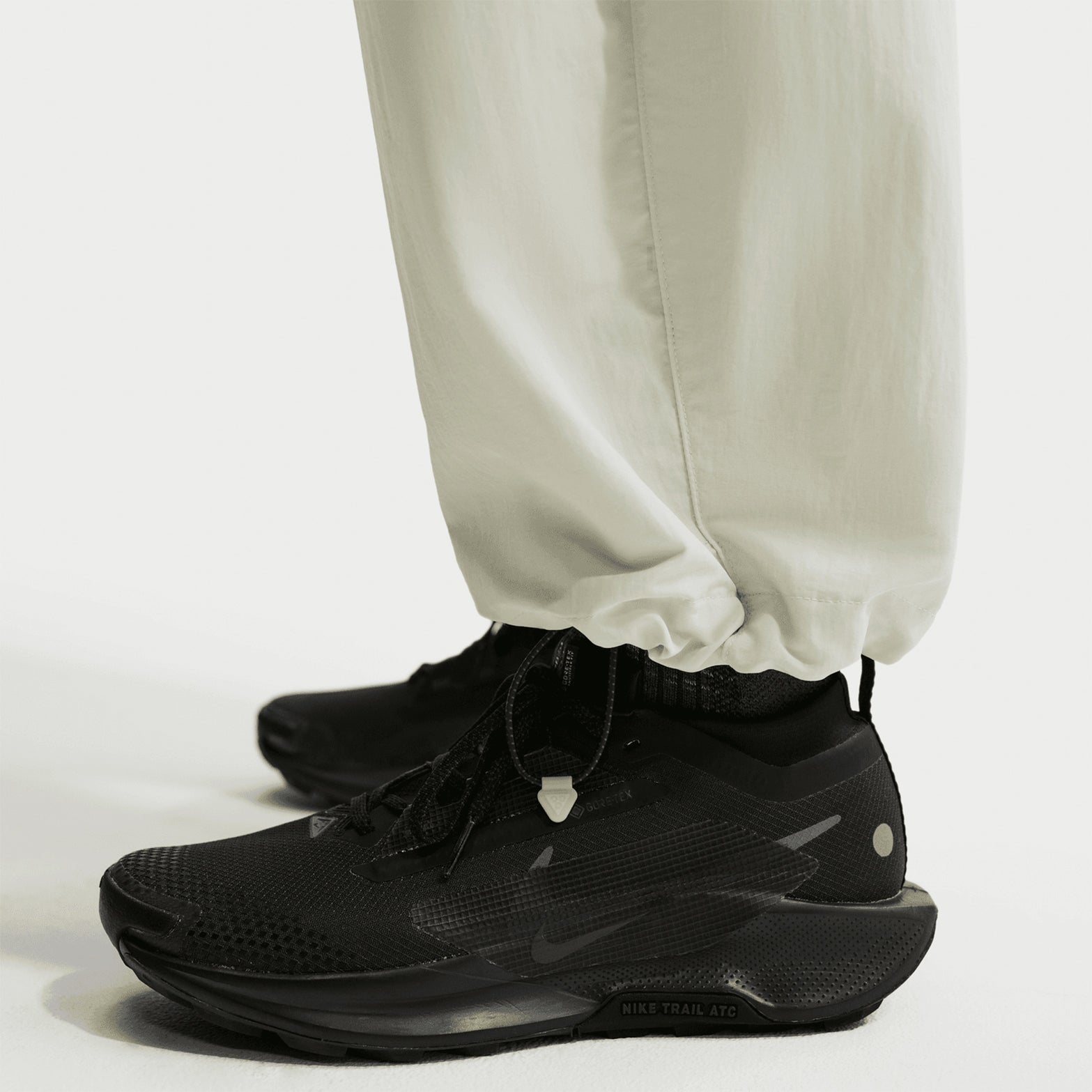 Nike ACG Dolomiti women's trousers in Sea Glass / Black — closeup showing sea glass adjustable bungee hem detail worn with ACG trail shoe, demonstrating customisable fit and practical terrain styling