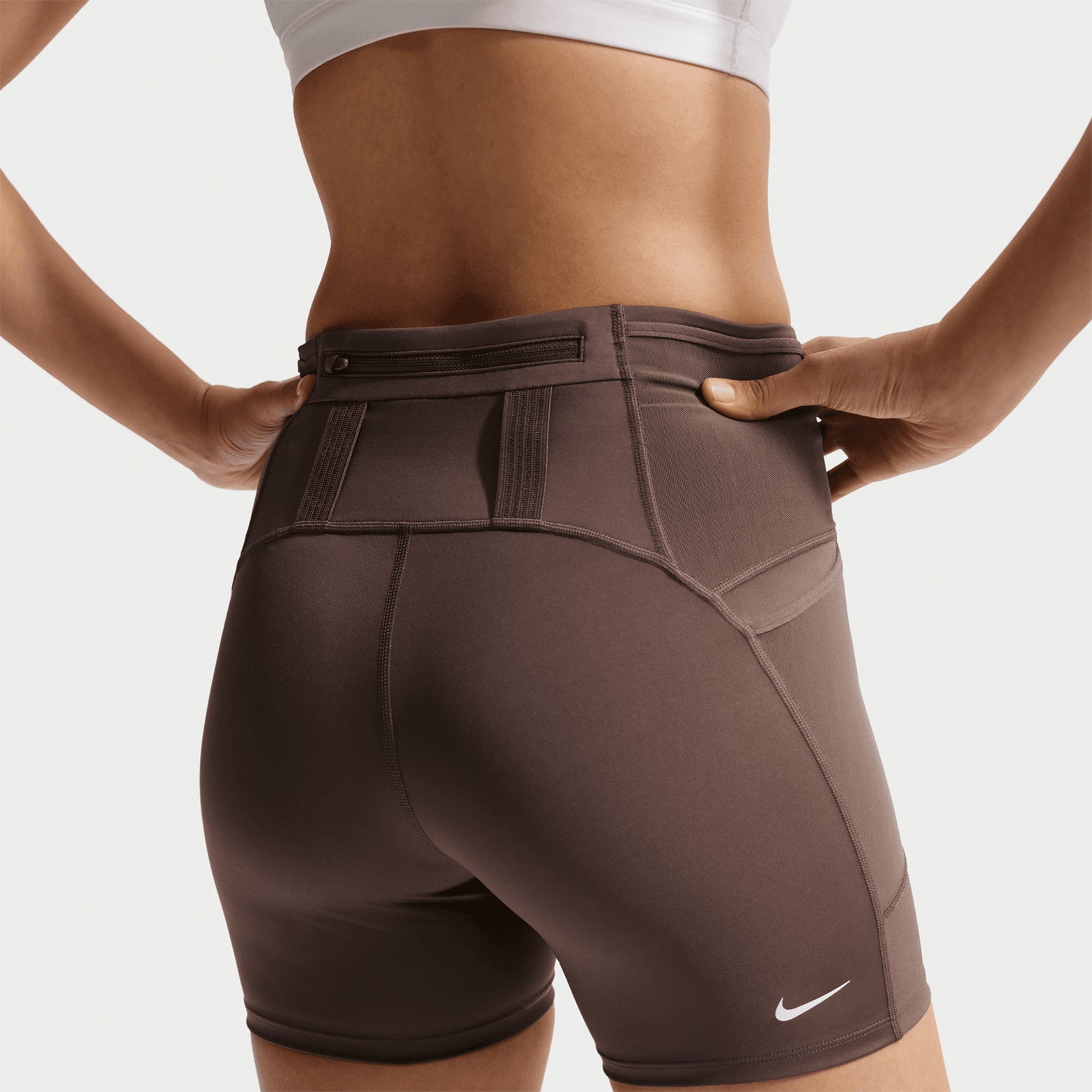 Women's Nike ACG High-Waisted 4 Inch Short Tights Ironstone Cave Stone Summit White back view on female runner showing back zip phone pocket and elastic loops for trekking poles or layers