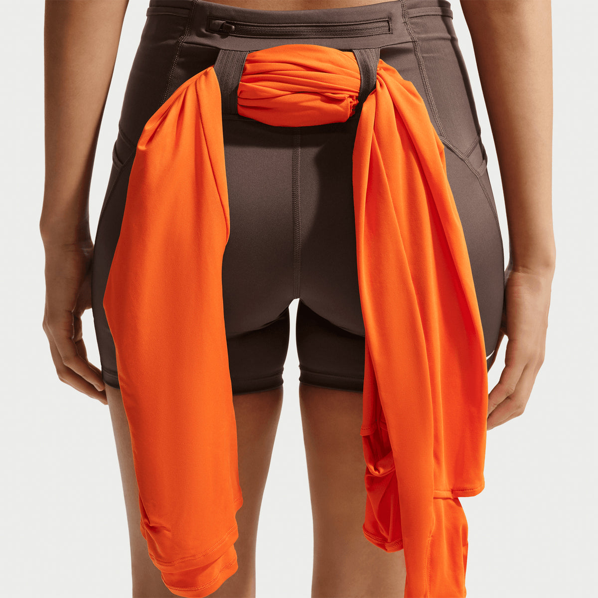Women's Nike ACG High-Waisted 4 Inch Short Tights Ironstone Cave Stone Summit White back full body view on female runner showing high-waisted coverage with elastic loops and zip pocket for trail running essentials