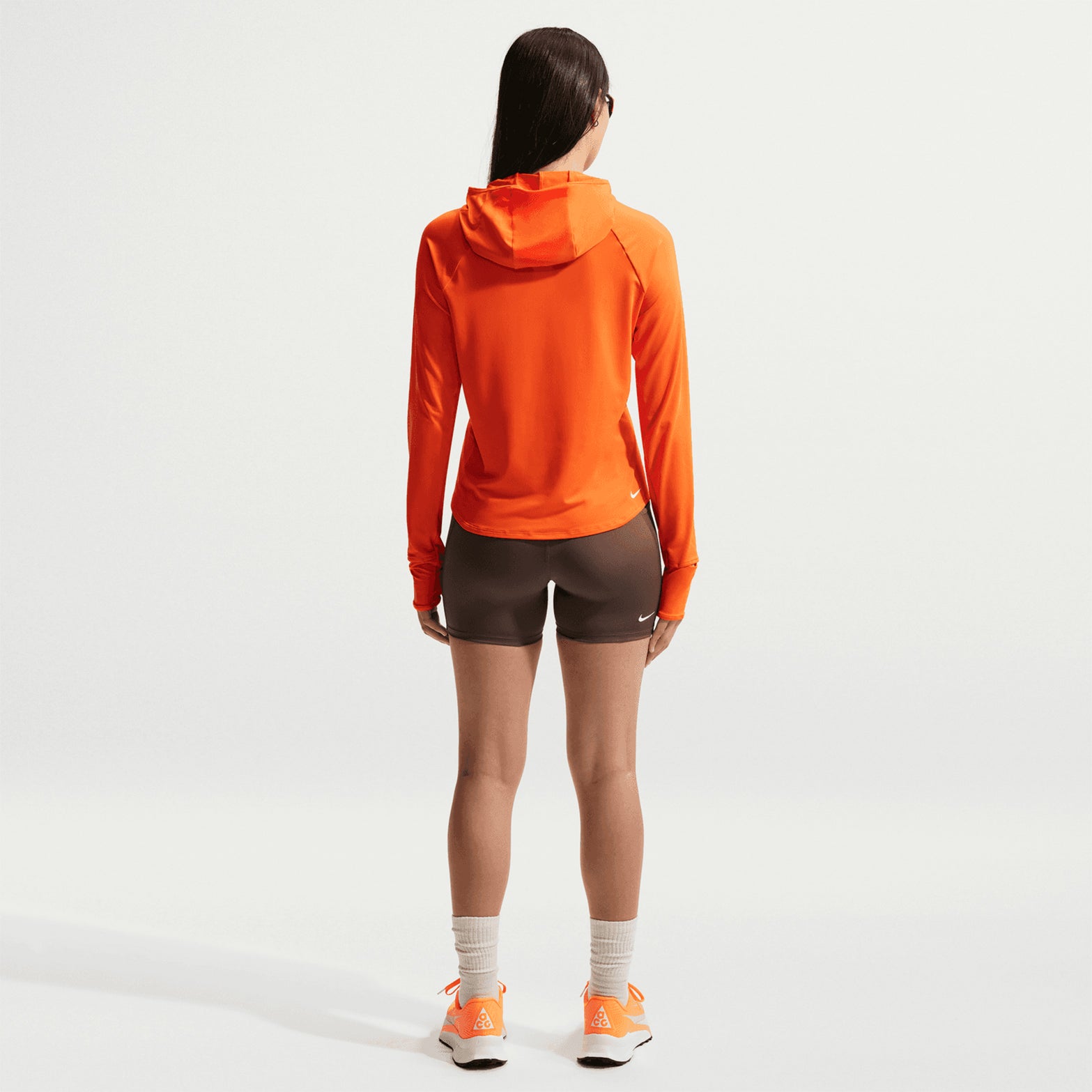Women's Nike ACG High-Waisted 4 Inch Short Tights Ironstone Cave Stone Summit White back full body view on female runner showing high-waisted coverage with elastic loops and zip pocket for trail running essentials