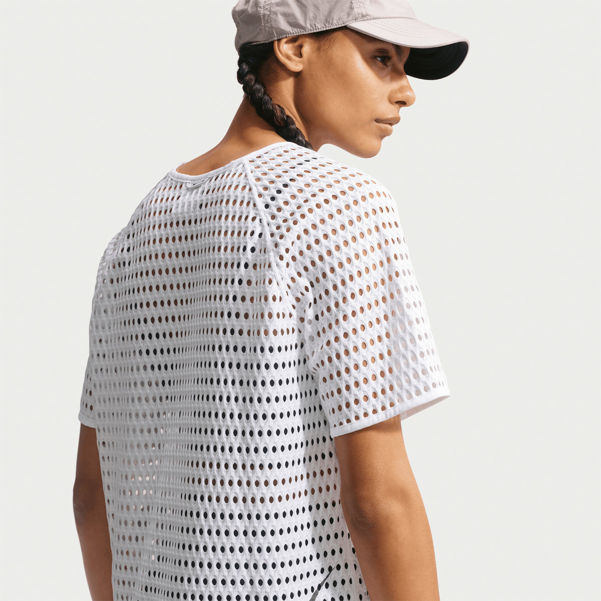A person wears a light-colored cap and the Nike Women’s ACG Radical AirFlow Tee White / Anthracite, glancing over their shoulder against a plain background.