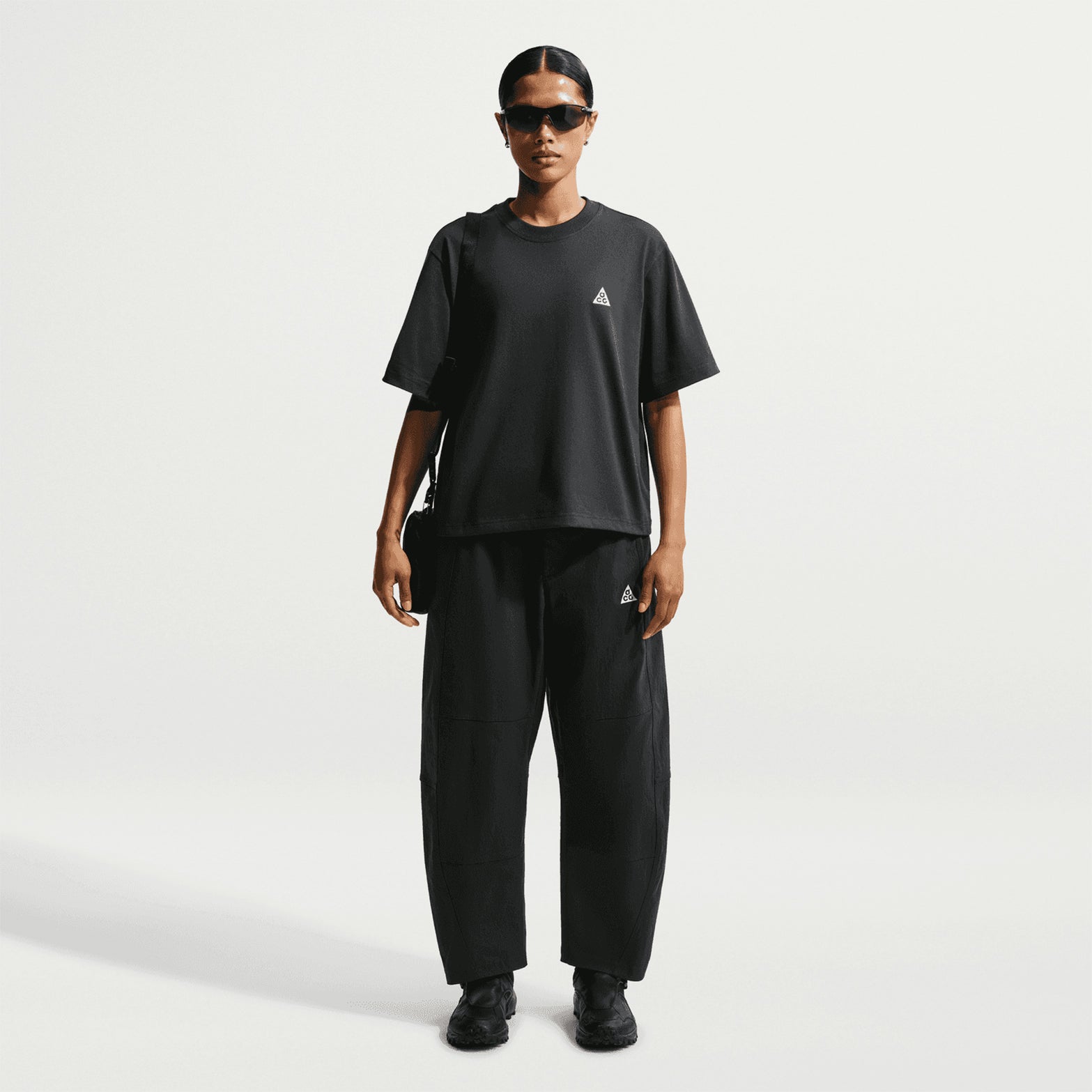 Nike ACG Tee women's in Black / Summit White — full body front view worn on model showing black loose-fit knit tee with summit white detailing, unrestricted silhouette and sustainable material construction