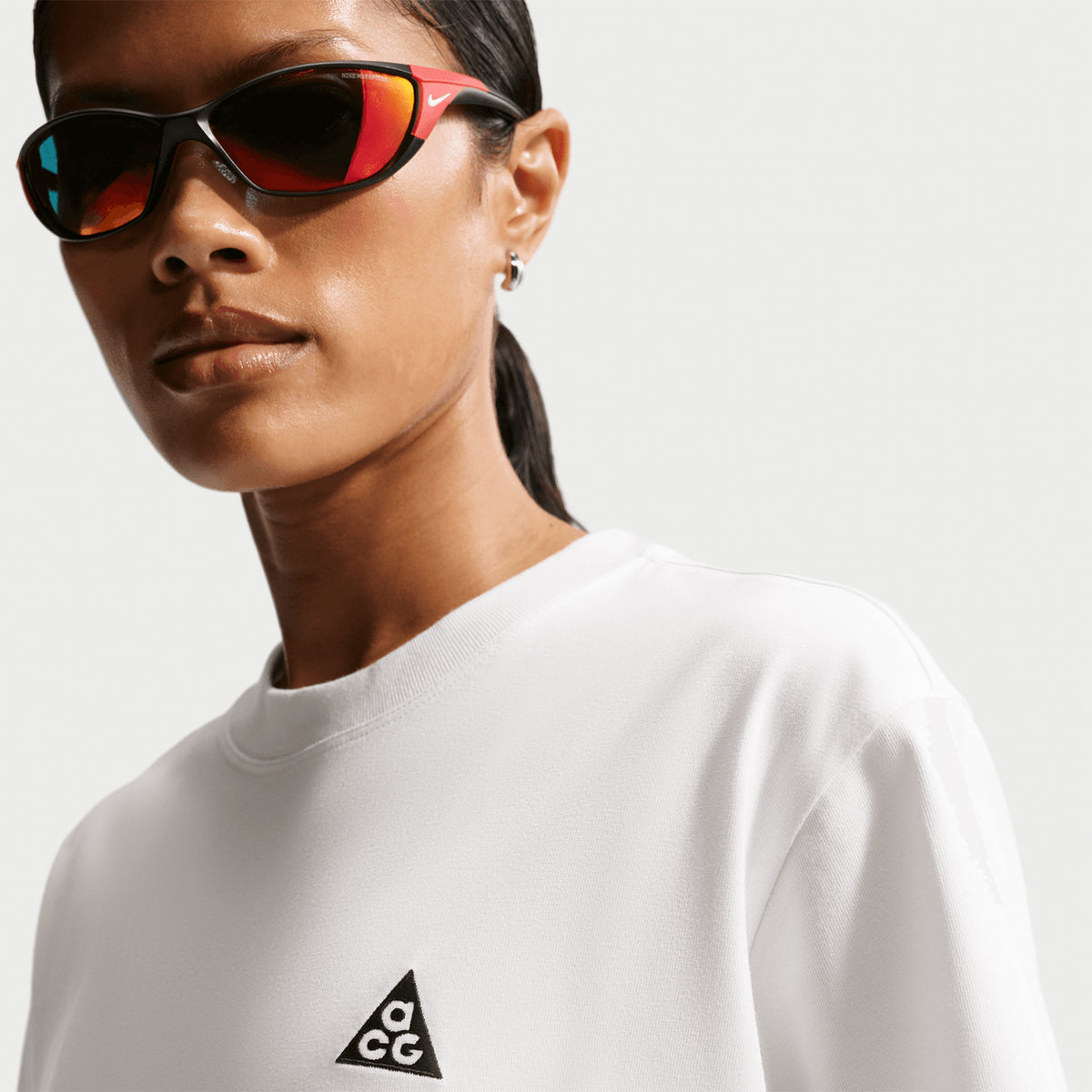 Nike ACG Tee women's in Summit White / Black — front closeup worn on model with sunglasses showing summit white knit fabric detail, black accent detailing and sustainable recycled polyester and organic cotton construction