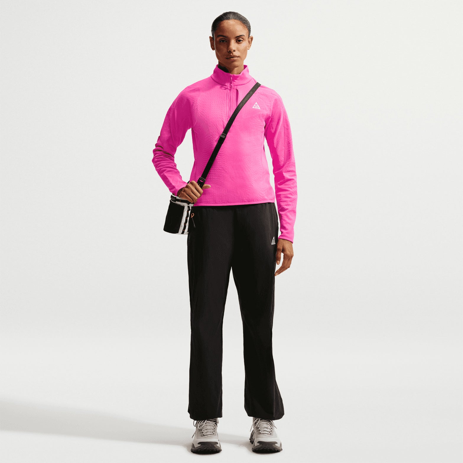 Women's Nike ACG Wolf Grid Therma-FIT 1/2 Zip Top Desert Pink Light Crimson Summit White full body view on female trail runner showing half-zip grid fleece with elastic hem and cuffs for warmth during mountain activities