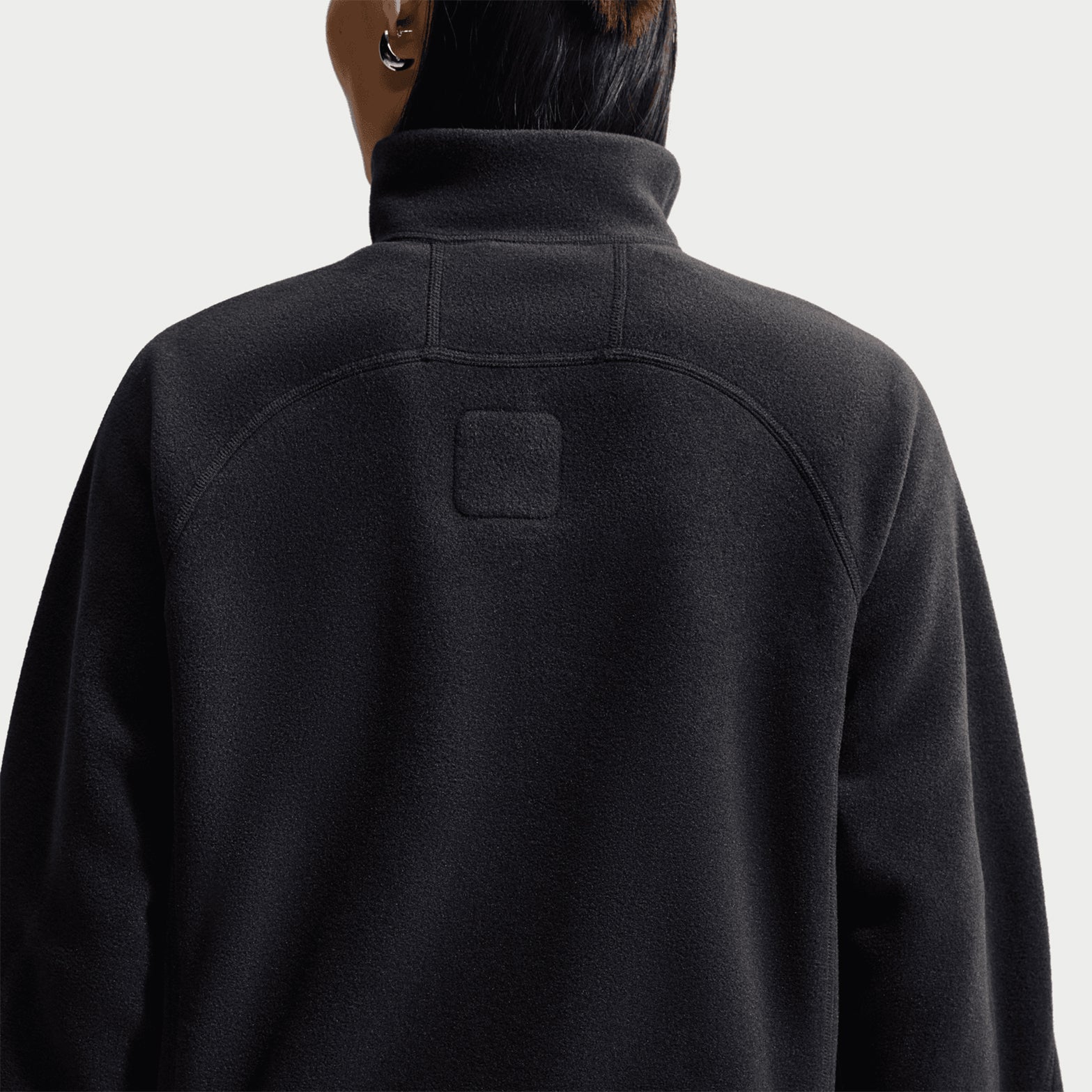 A person is shown from the back wearing the Nike Women’s ACG Wolf Tree 1/2 Zip Top in Black / Anthracite / Summit White, featuring a high collar and a small rectangular patch at the upper center. The plain white background highlights this trail-ready essential.