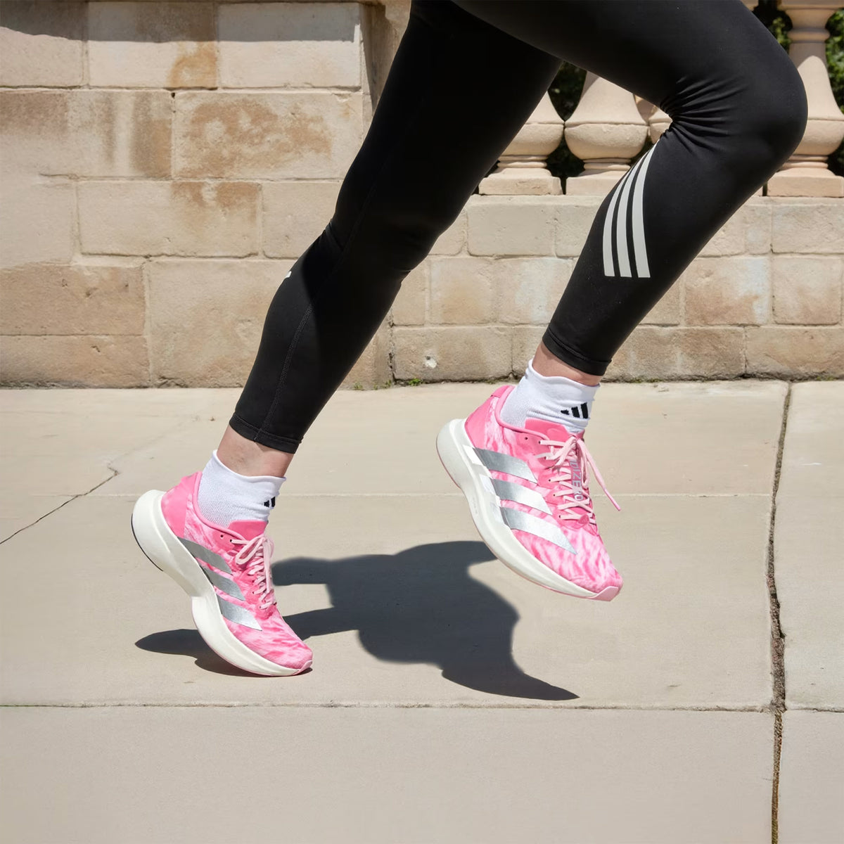 adidas Adizero EVO SL Woven women's running shoe in Pink Fusion / Silver Metallic / Clear Pink — side view worn in motion, showing pink fusion woven upper with silver metallic 3-Stripes and LightstrikePro midsole profile