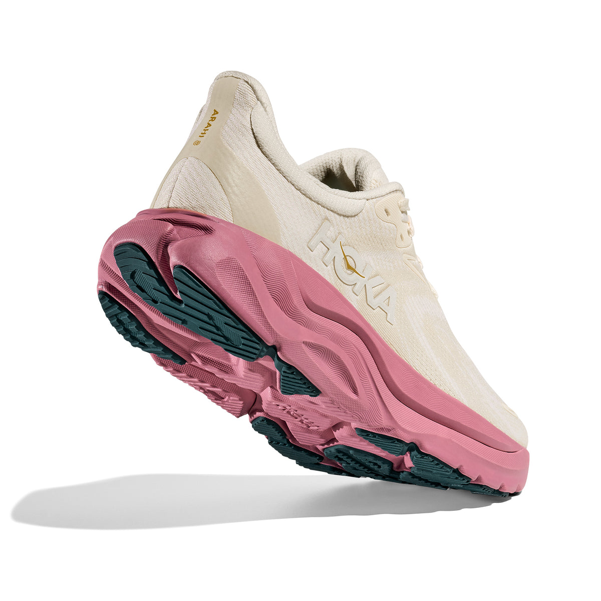 A beige HOKA running shoe with a thick pink and green sole is shown angled upward on a white background, highlighting its cushioning and tread design.