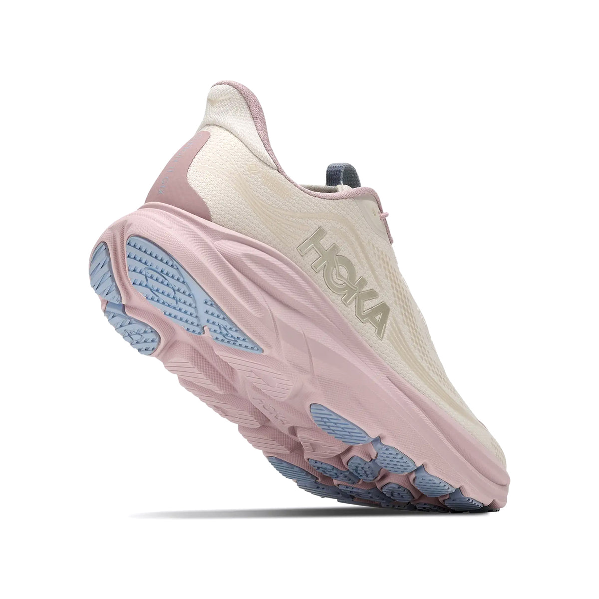 A light pink and cream athletic shoe with a thick sole, light blue tread, and HOKA branding on the side, shown from a low rear angle on a white background.