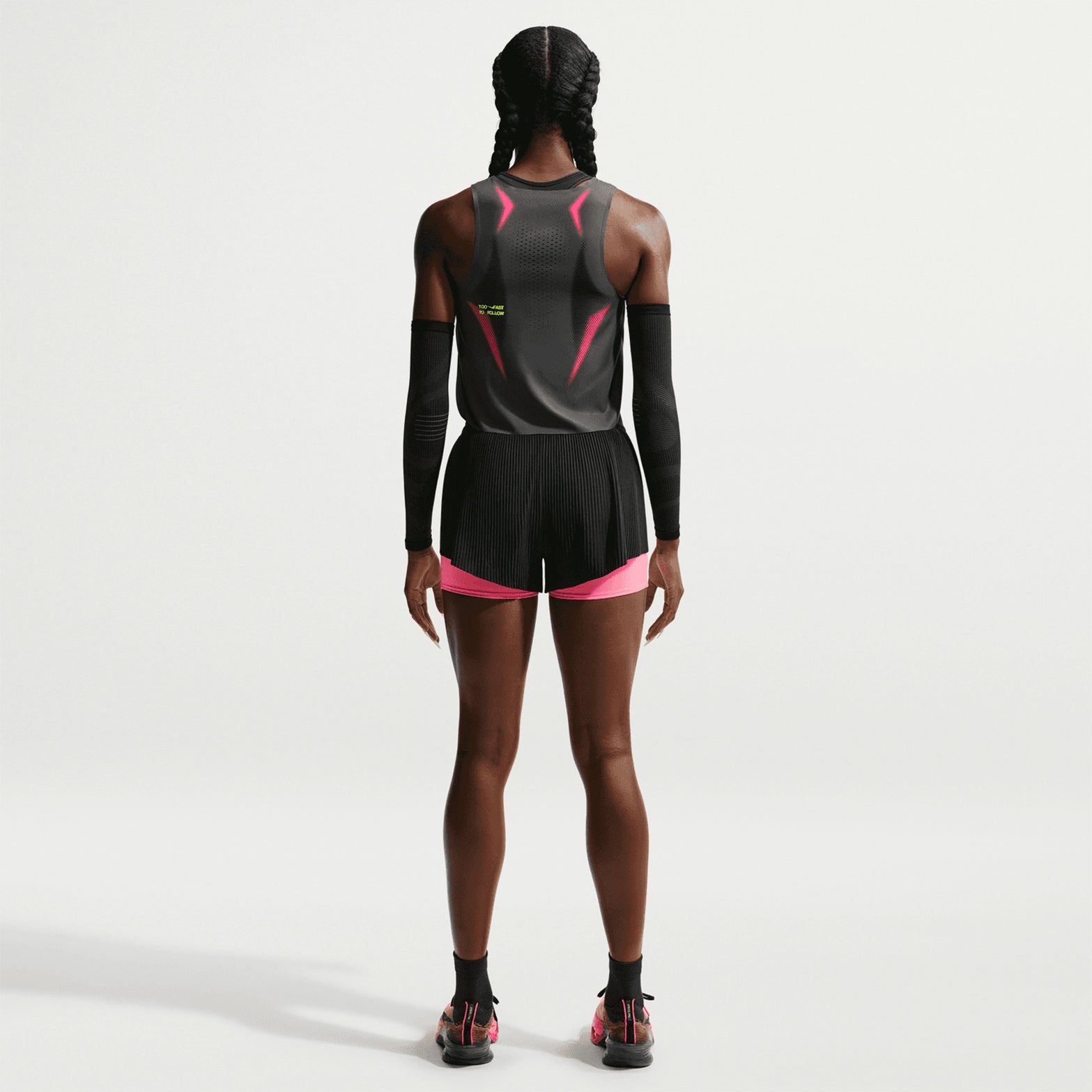 A woman with braided hair stands facing away, wearing a Nike Women’s Dri-FIT ADV Cropped Running Vest in Iron Grey, Volt, and White.