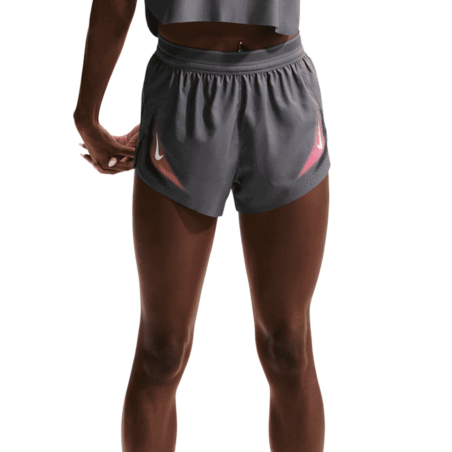A person stands facing away, wearing Nike Women’s Dri-FIT Aeroswift ADV 3 Inch Running Shorts in Iron Grey and White, paired with a cropped gray top. The background is white.