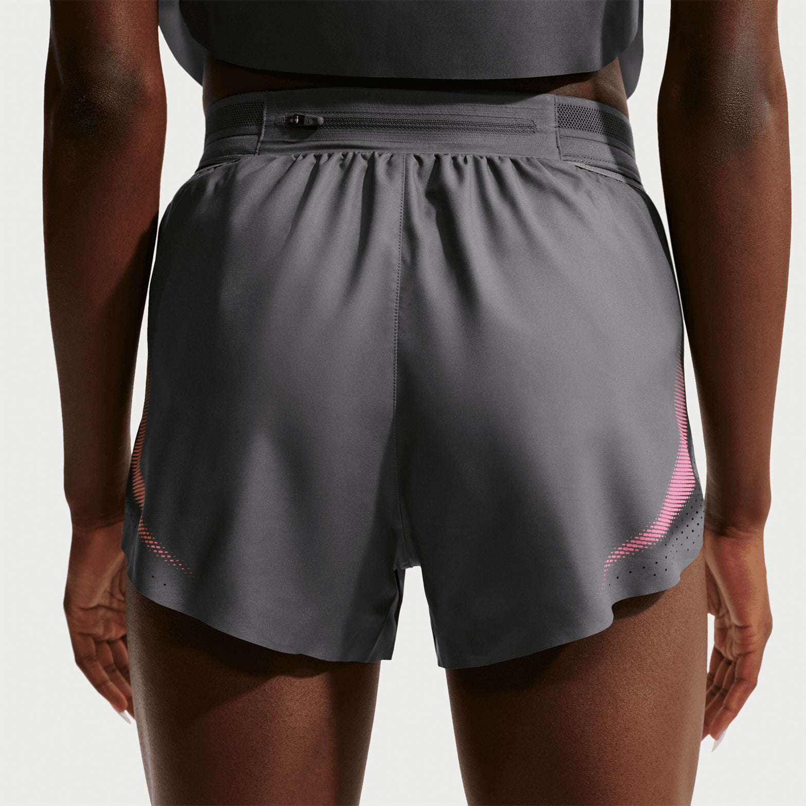 A person is shown from the back against a plain light background wearing Nike Women’s Dri-FIT Aeroswift ADV 3 Inch Running Shorts in Iron Grey and White. These lightweight performance running shorts feature an elastic waistband and a small zipper pocket at the top, providing both comfort and functionality.