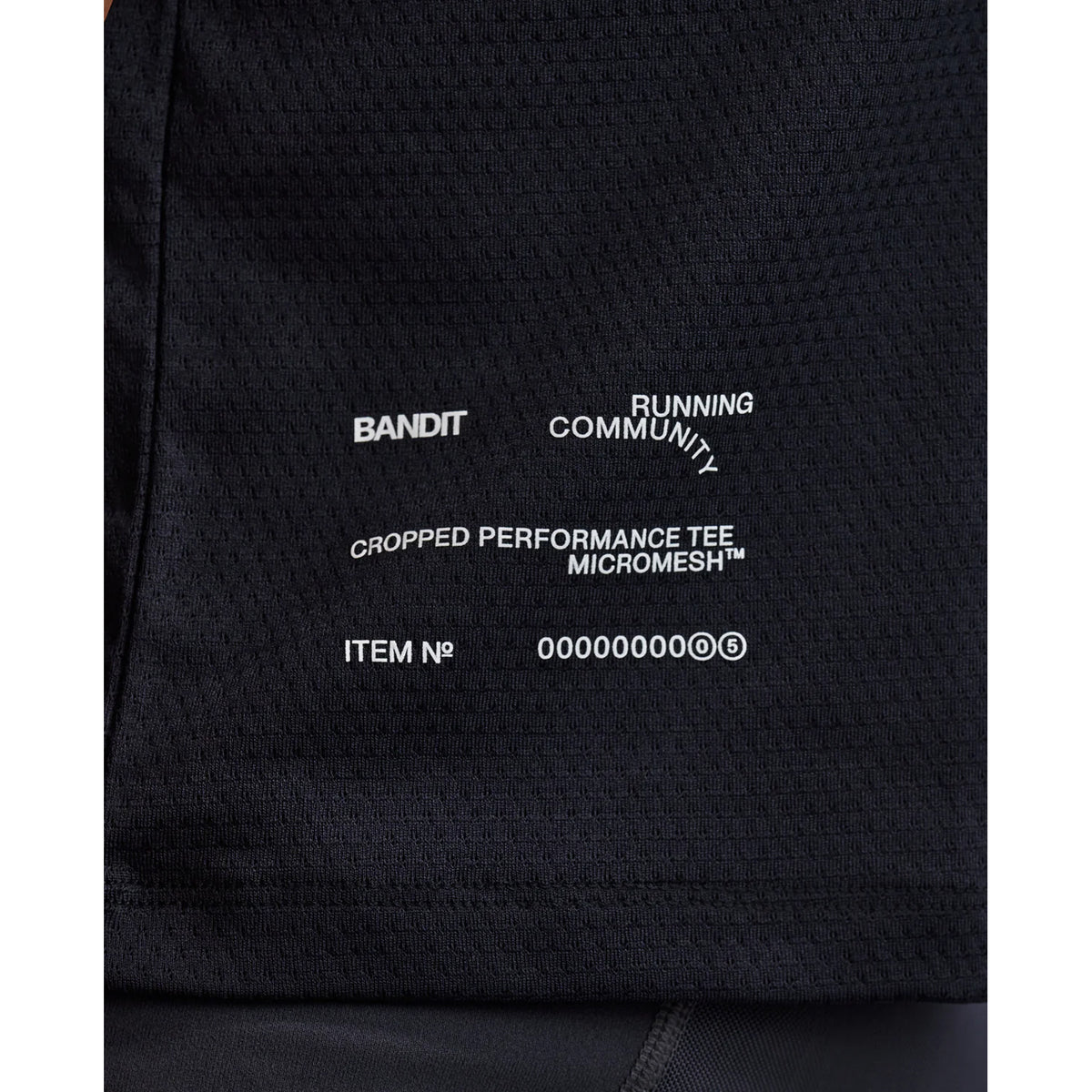 Women's Bandit Micromesh Cropped Run Tee Black close-up of hem showing subtle two-tone Bandit logo with reflective details for low-light visibility during running