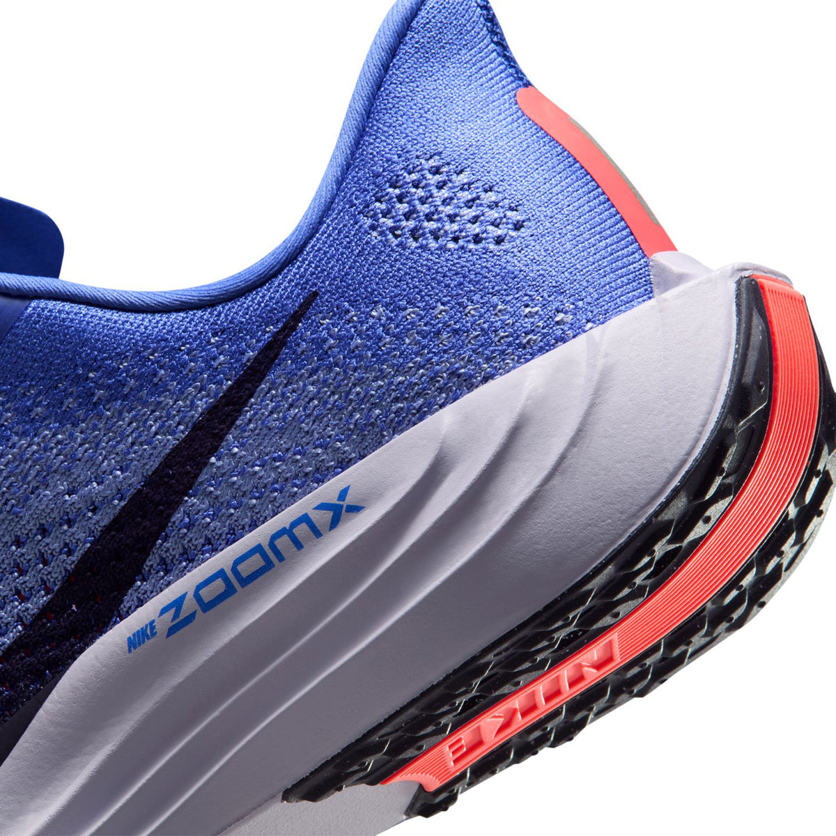 Close-up of a blue Nike running shoe, showing the heel and part of the sole with ZOOMX text, black and red accents, and the Nike logo on the outsole.