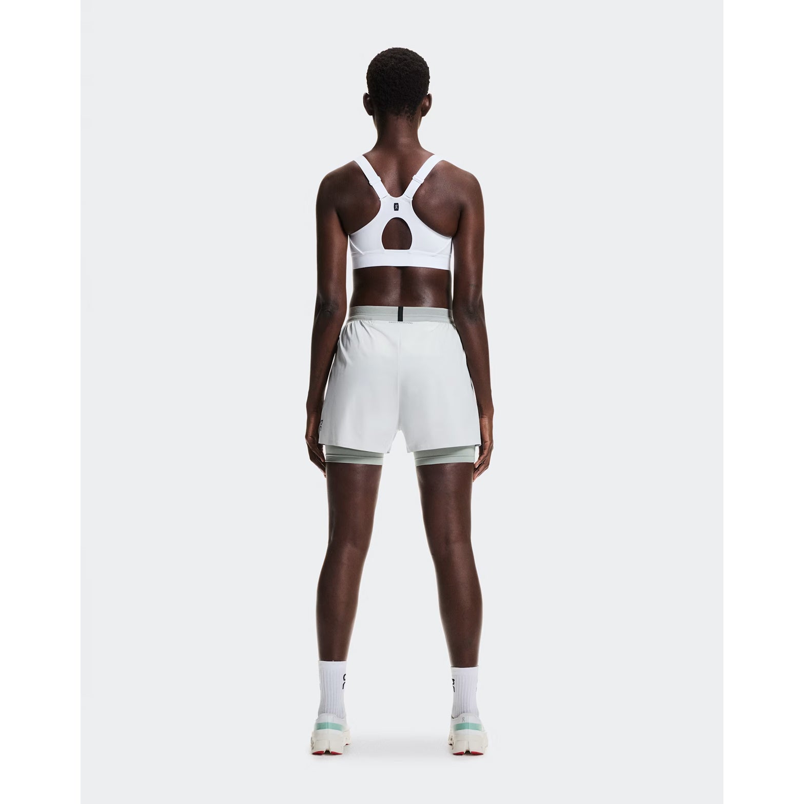 Women's On Performance Bra White full body back view on female runner showing mesh racerback inserts for breathability and adjustable straps with back-positioned adjusters for comfort