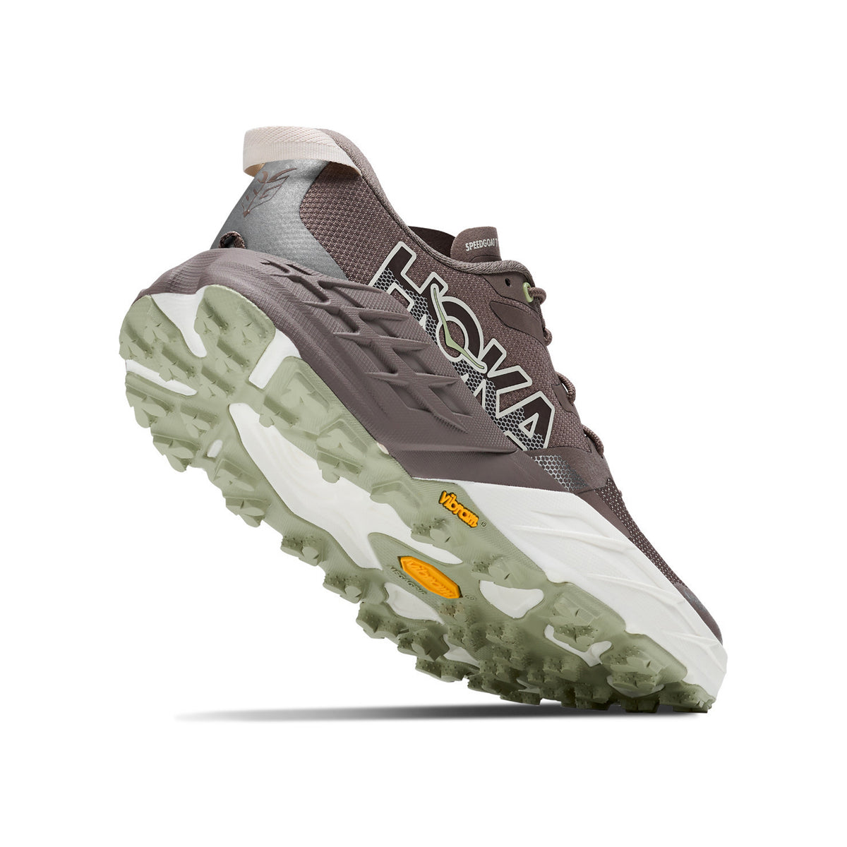 Brown and gray Hoka trail running shoe angled to show the rugged, translucent green sole with white and yellow accents. The shoes logo is visible on the side.