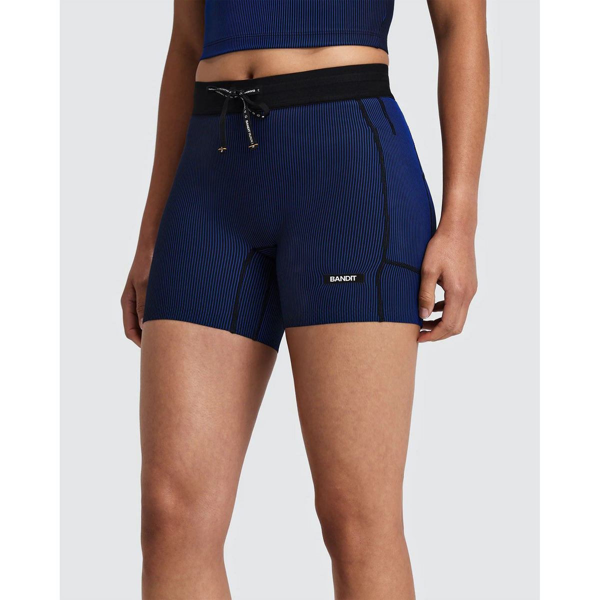Person wearing Women’s Striped Cadence 5″ Compression Shorts Black / Bauhaus Blue, which are ultra-compressive blue ribbed compression shorts featuring a black waistband and drawstring.