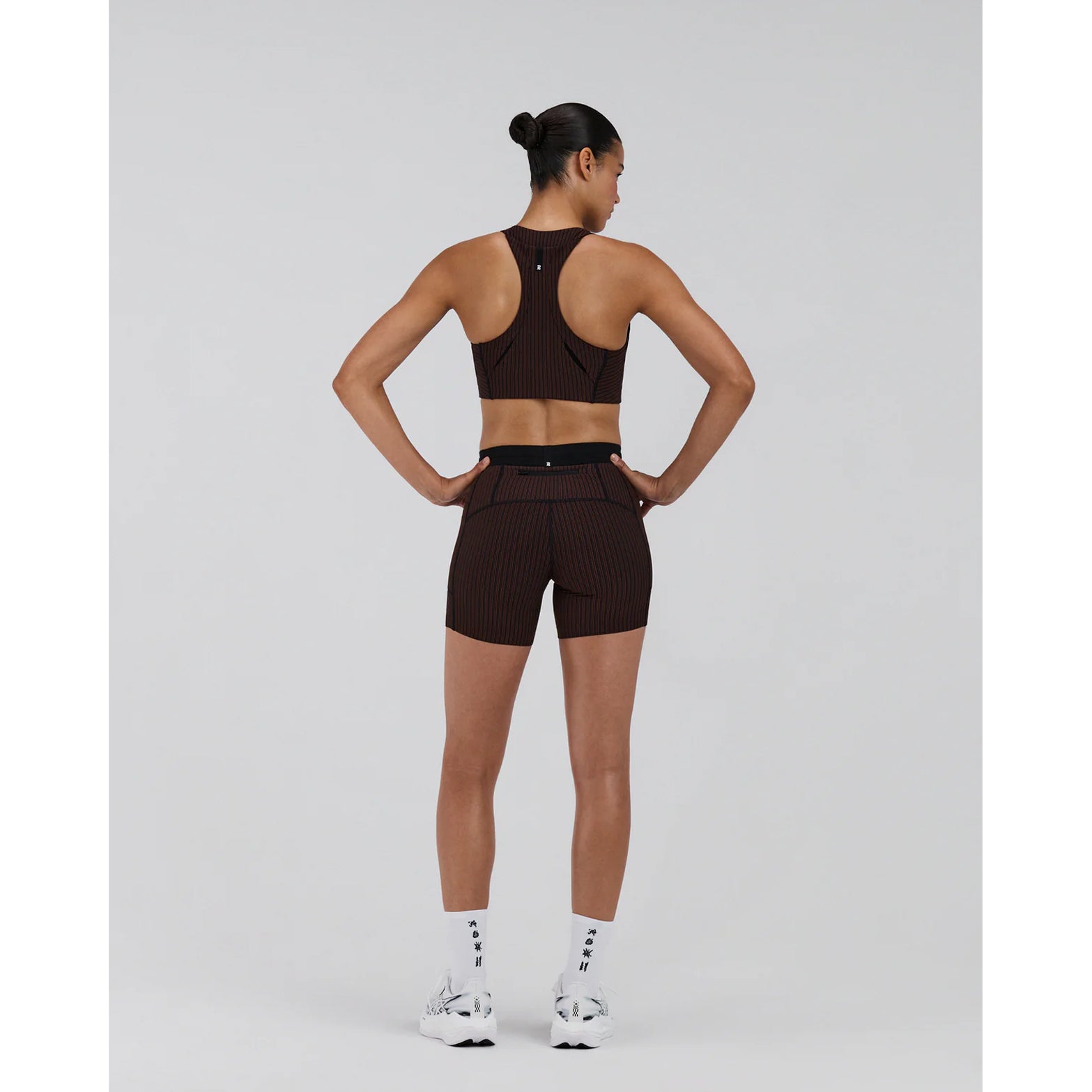 Bandit Striped Cadence Longline Bra women's in Cacao / Black — full body back view worn on model showing T-shirt loop detail at centre back, underarm gel pocket placement and cacao and black striped ribbed knit fit in motion