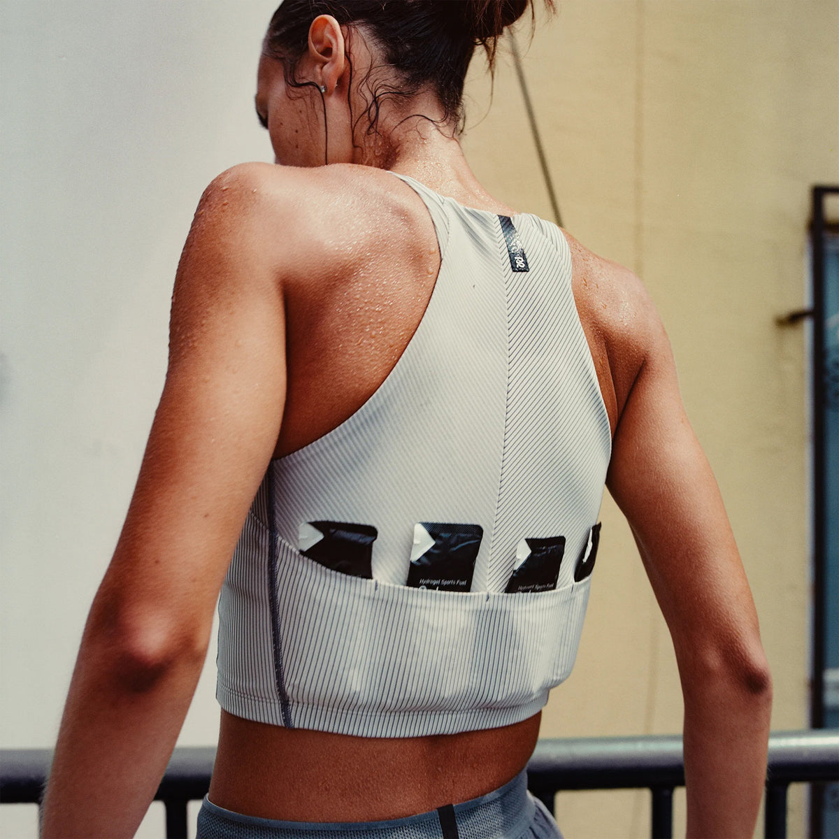 Women's Bandit Striped Cadence Zip Front Race Crop Plaster Slate lifestyle shot showing seven-pocket system in use with three waterproof phone pockets and four gel pockets designed to disappear during racing and training