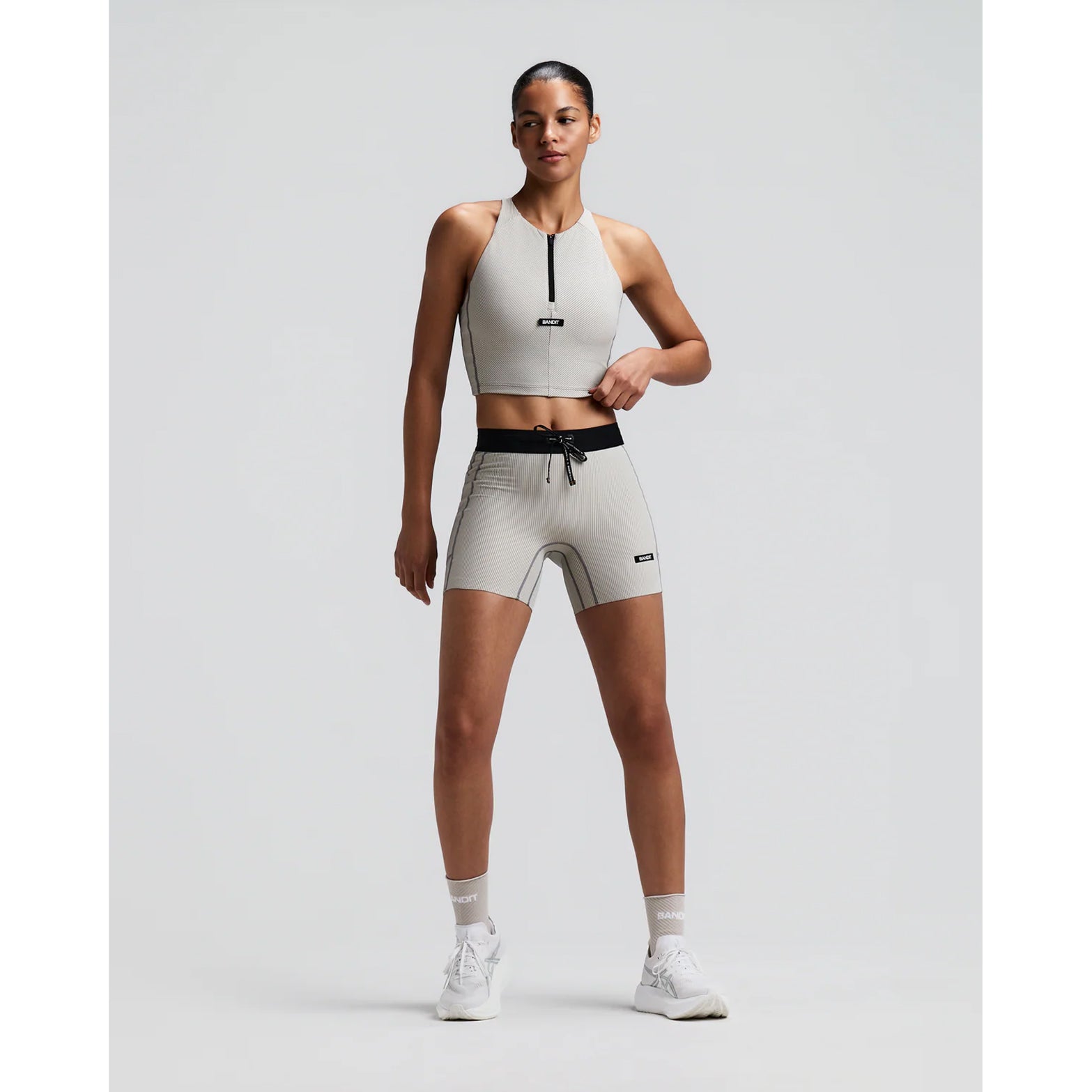 Women's Bandit Striped Cadence Zip Front Race Crop Plaster Slate front full body view on female runner showing halter fit with zip front, Striped Cadence ribbed compression and seven-pocket system for road running and racing