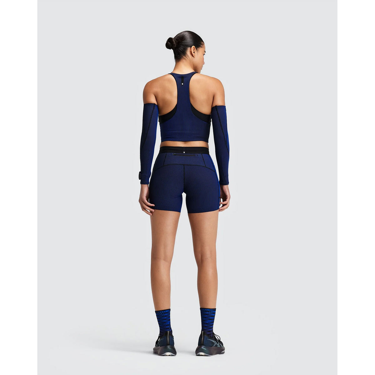 Back view of a person wearing a Women’s Striped Cadence Zip Front T-Back Race Crop Black / Bauhaus Blue, featuring a ribbed compression design with matching athletic shorts and separate arm sleeves.