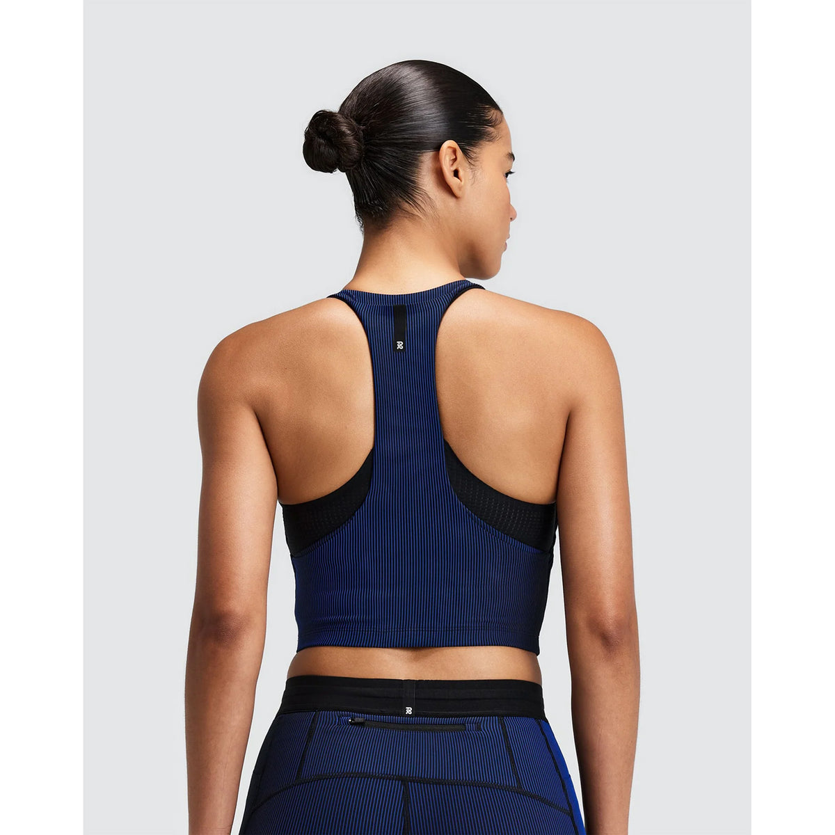 Back view of a woman wearing a navy blue and black Women’s Striped Cadence Zip Front T-Back Race Crop over a black sports bra.