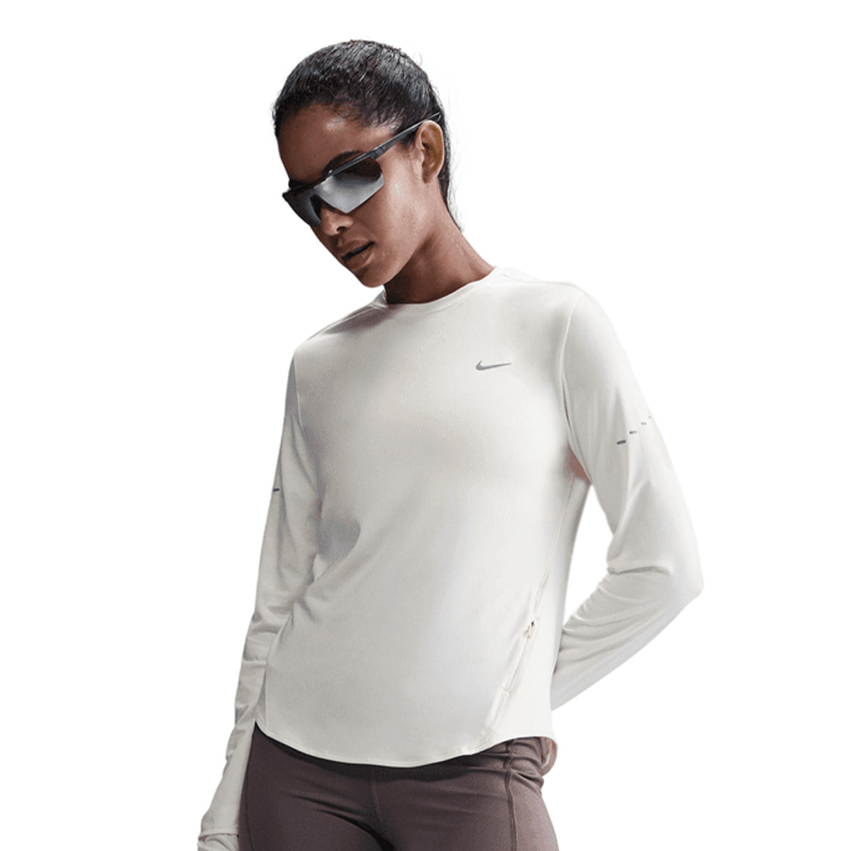 A woman wearing sunglasses, the Nike Women’s Swift Dri-FIT UV Crew-Neck Running Top in Sail, and brown pants poses against a plain background.
