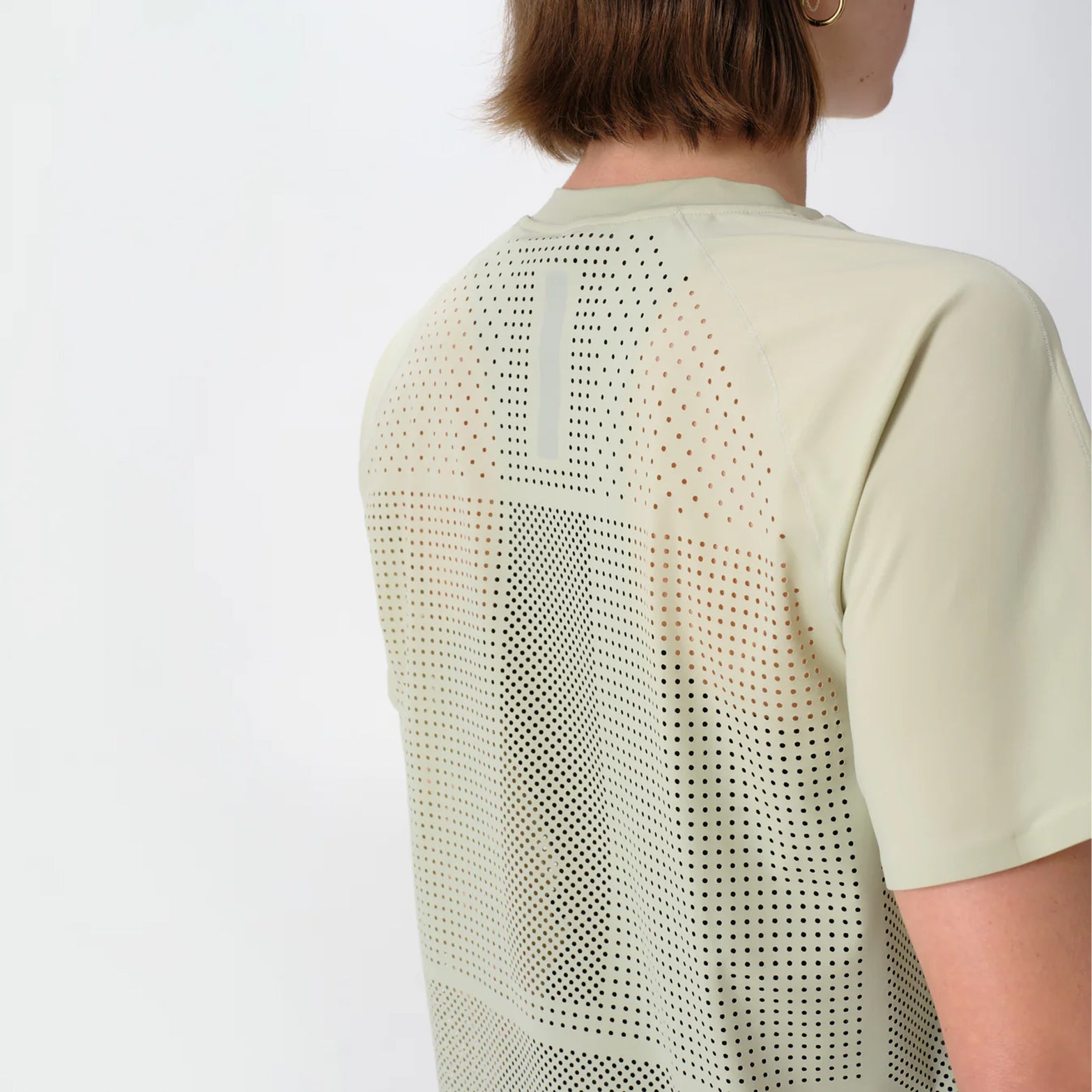 Women's Raide Thermal Dispersion Tee Lichen back view on female runner showing densely perforated centre back heat zone with body-mapped laser-cut ventilation for evaporative cooling during sustained efforts
