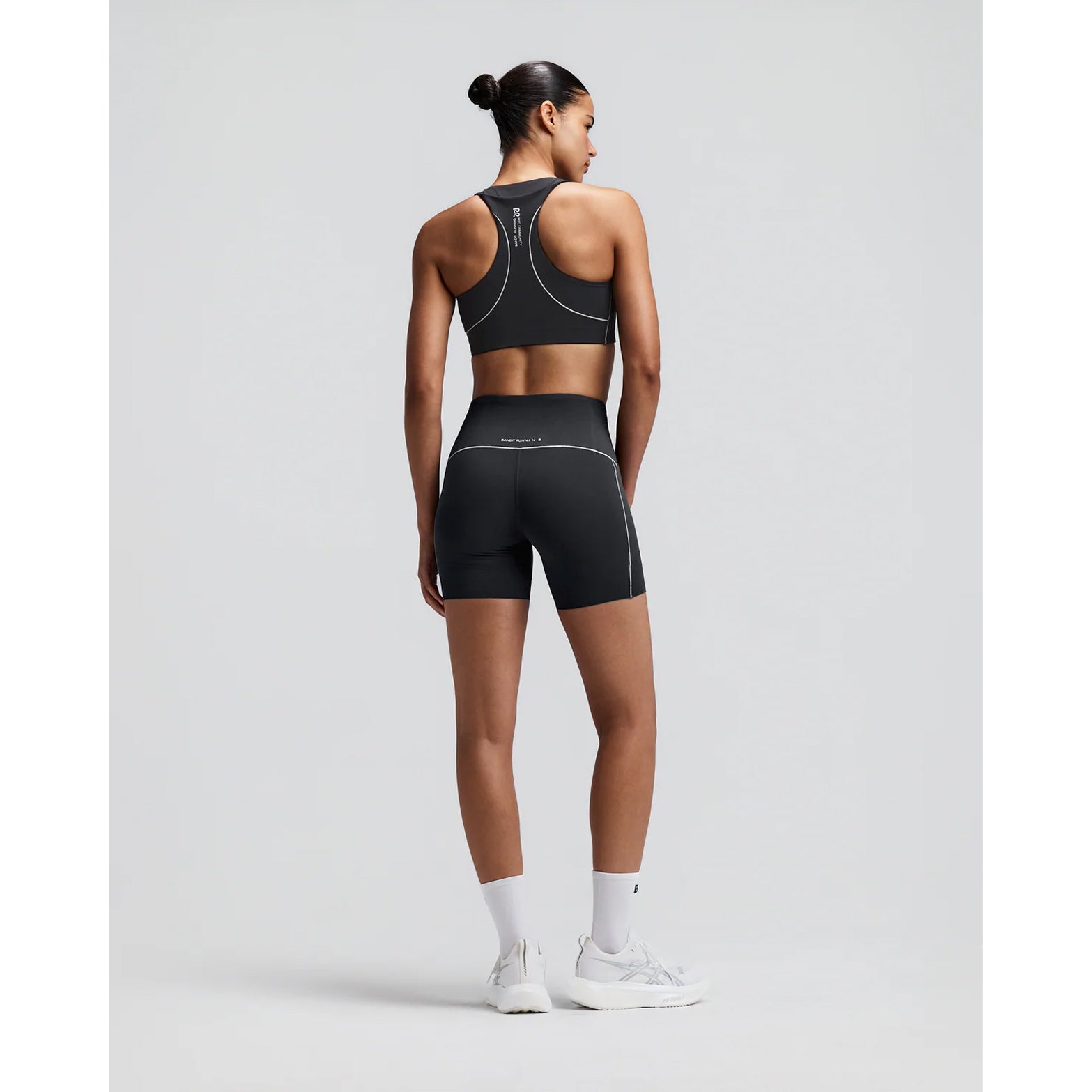 Women's Bandit Vanisher Pop Stitch Arco Run Bra Anthracite back full body view on female runner showing waterproof back phone pocket with reflective branding and Vanisher compression for comfortable running